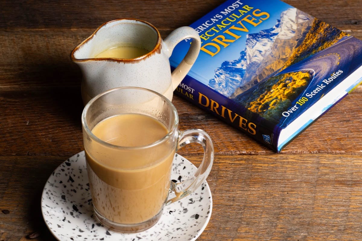 Butterscotch coffee creamer in a vessel with a mug of coffee and a book on a wooden table.