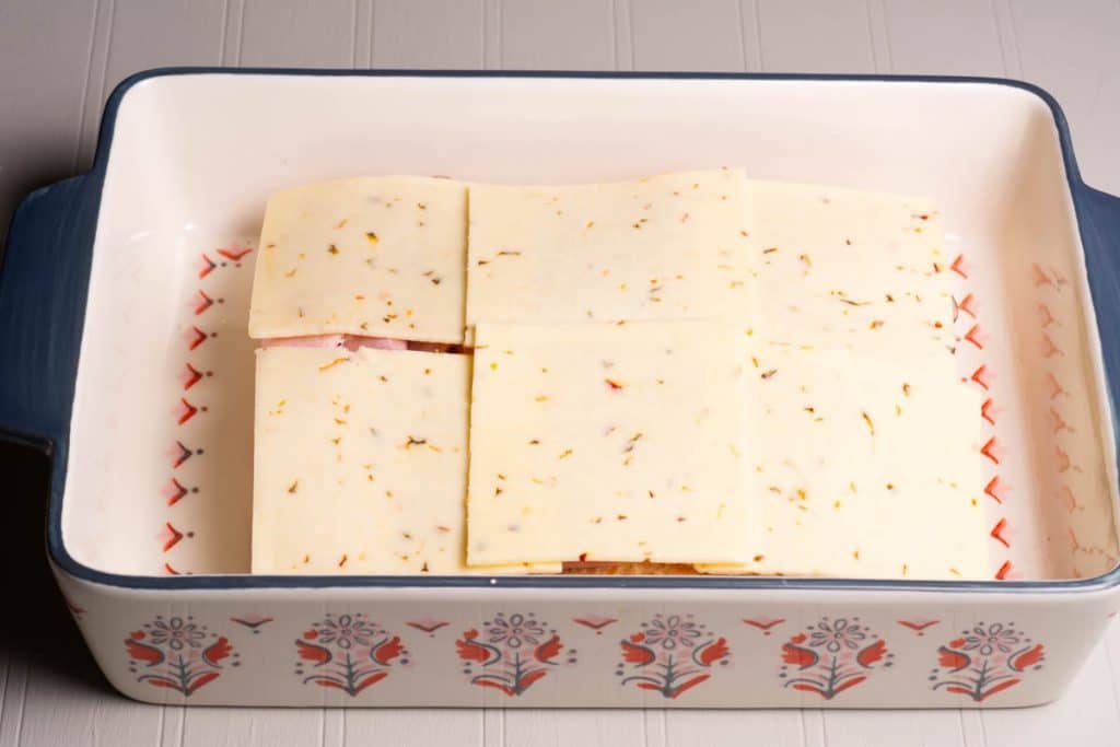 A rectangular cake pan with Hawaiian rolls topped with ham and cheese slices.