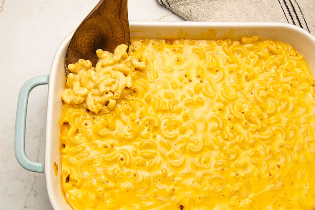 A rectangular baking dish full of Velveeta baked mac and cheese with a wooden spoon.