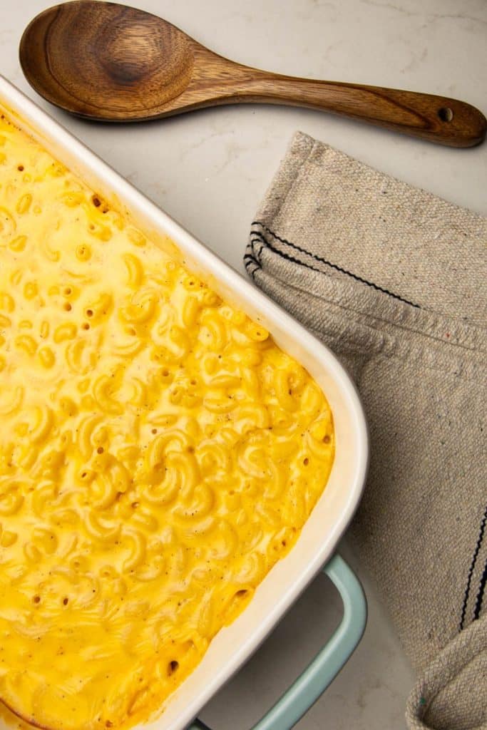 Baked macaroni and cheese with Velveeta in a baking dish with a wooden spoon and kitchen towel.