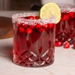 Glass of cranberry margarita with a salted rim on a marbled table.