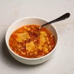 One-pot lasagna soup in a white bowl on a marbled table with a spoon in the bowl.