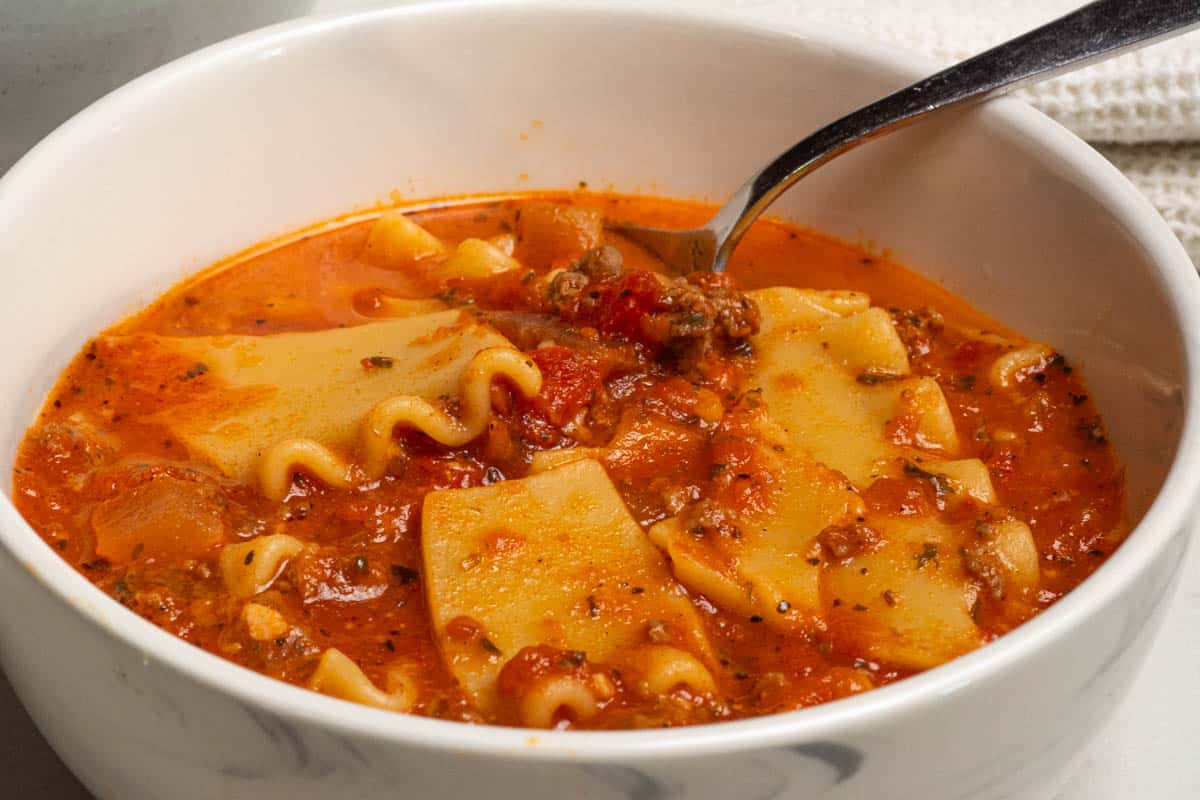 A white bowl of one pot lasagna soup with a spoon in the bowl.