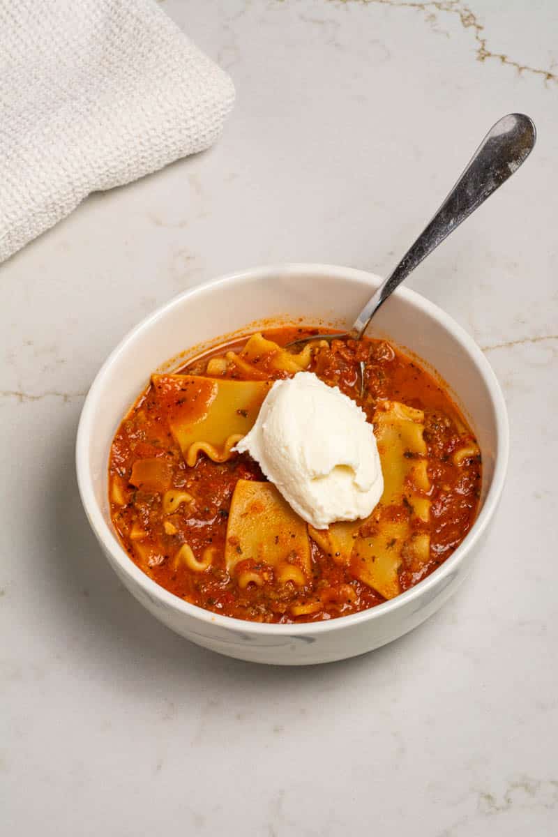 One-pot lasagna soup in a white bowl with a dollop of ricotta cheese.