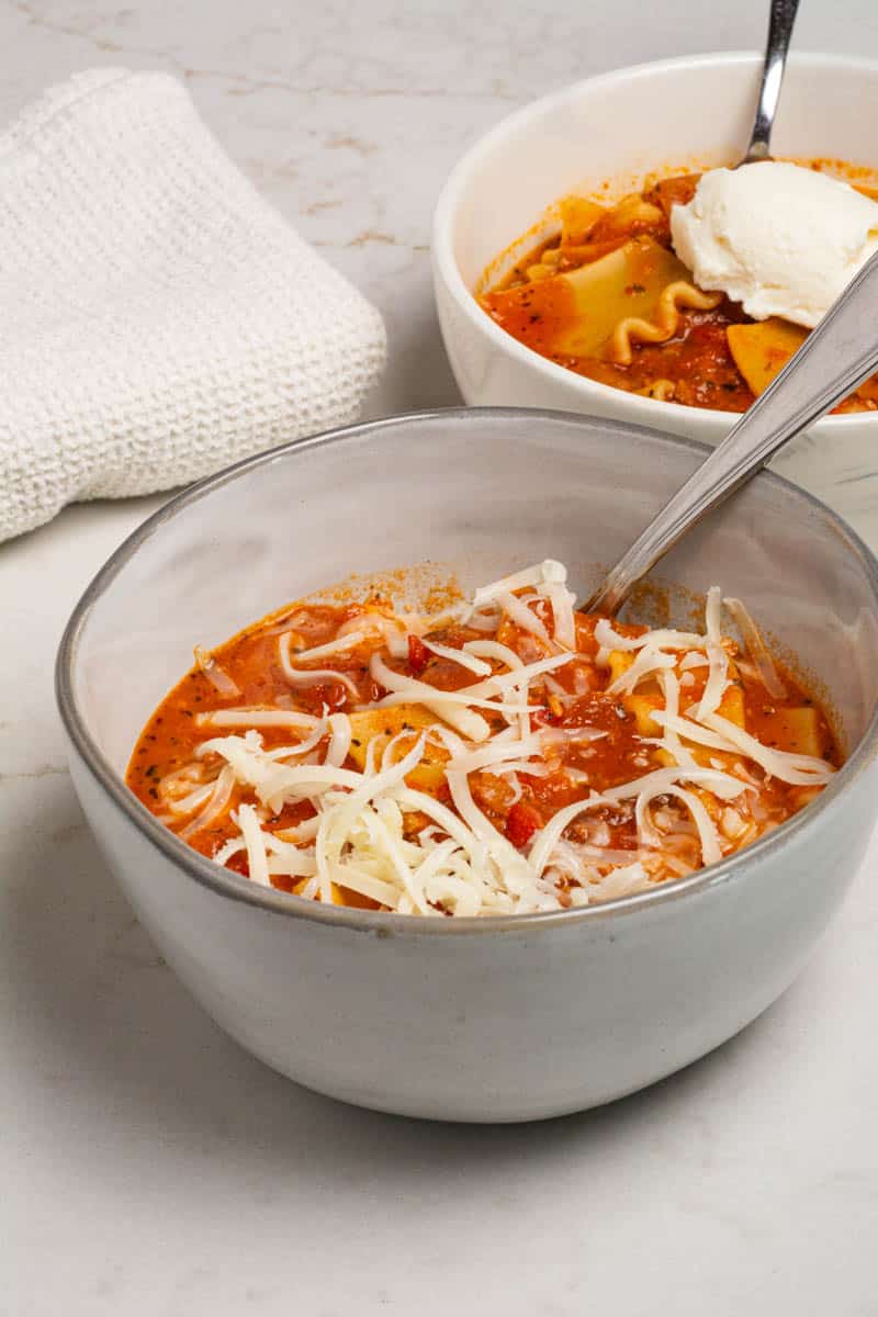 Two rounds bowls filled with one-pot lasagna soup. One has a dollop of ricotta and the other has shredded mozzarella.