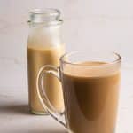 A clear glass with coffee and a glass bottle of peppermint coffee creamer.