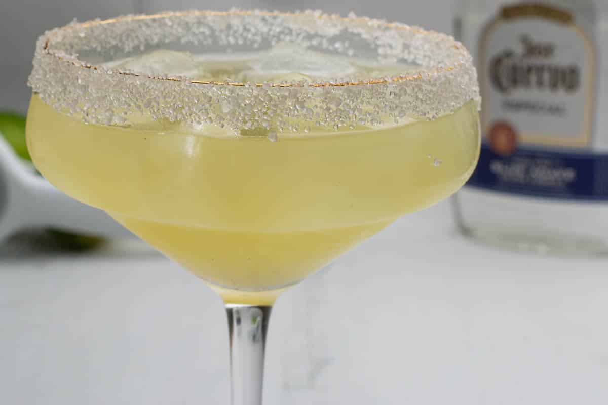 A close up photo of an agave margarita with a bottle of tequila in the background.