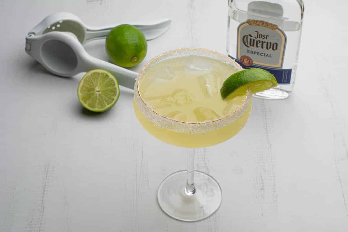 A agave margarita in a margarita glass with a lime wedge.