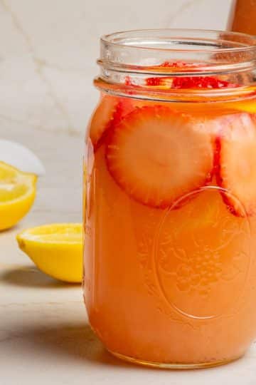 Homemade strawberry lemonade in a pint mason jar with strawberry and lemon garnish.