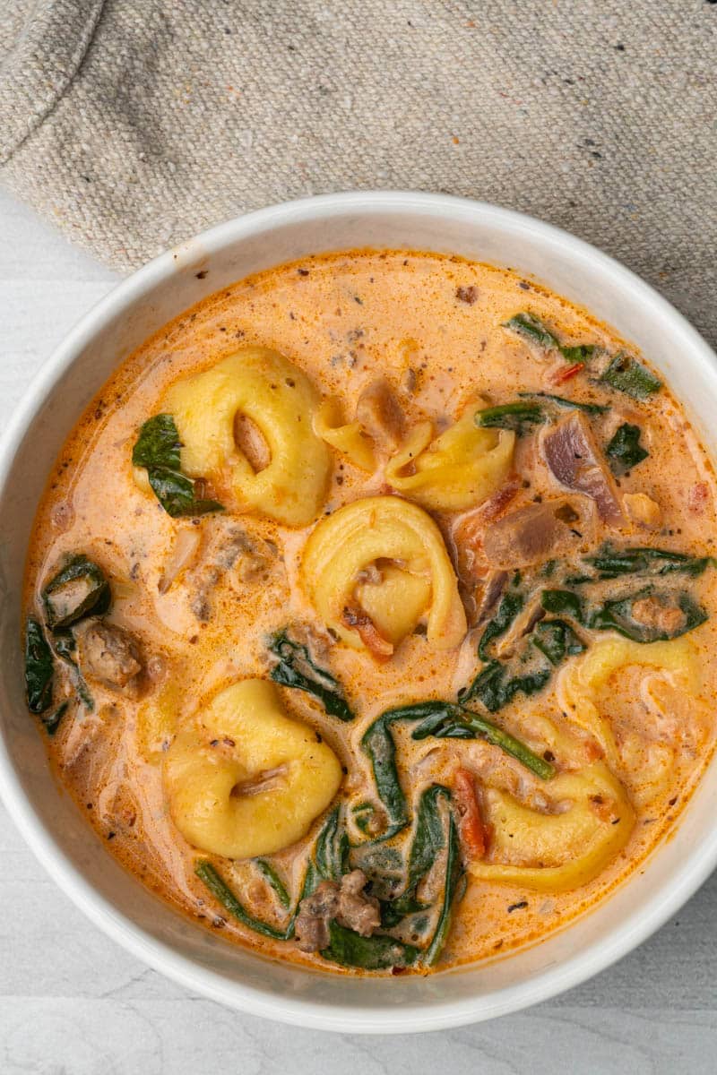A white bowl filled with tortellini soup with sausage and spinach.