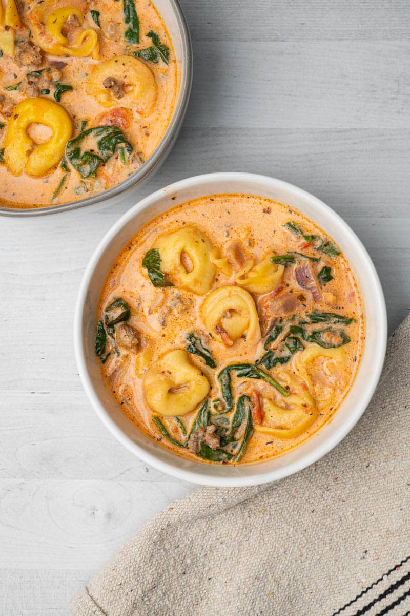 Overhead photo of two bowls of tortellini soup with sausage and spinach.