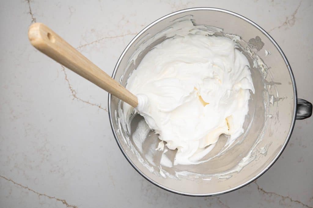 A mixing bowl full of a cream cheese, powdered sugar, and a Cool Whip mixture.
