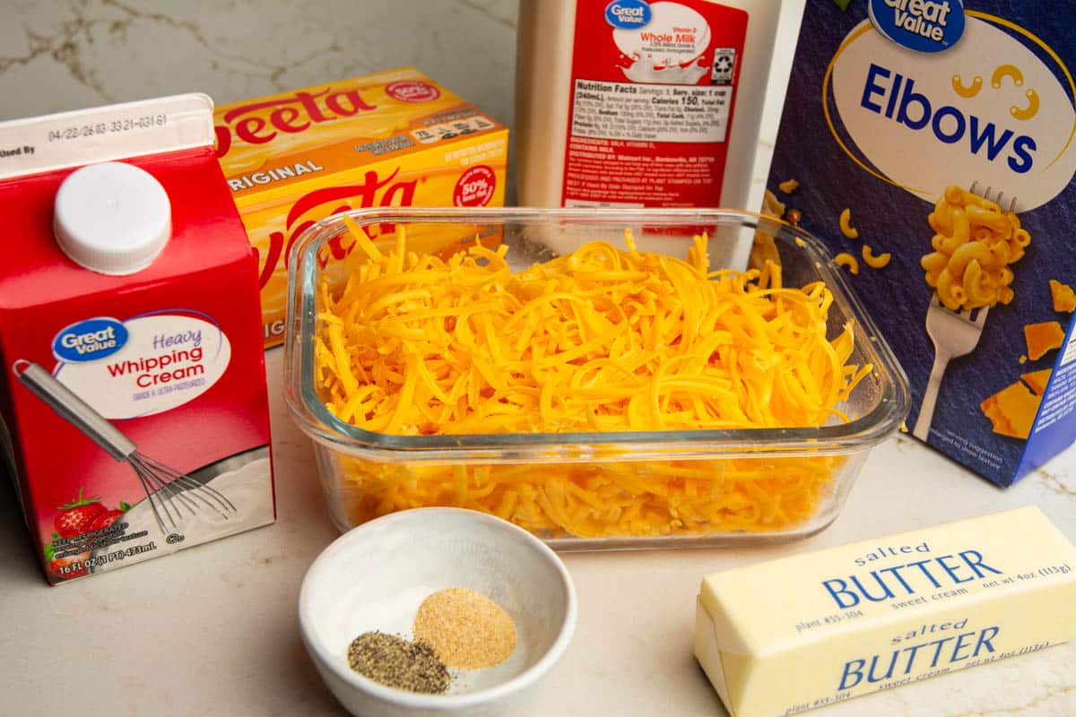 Ingredients for a macaroni and cheese with Velveeta recipe. The phot has heavy cream, seasonings, butter, Velveeta, elbow macaroni and milk.