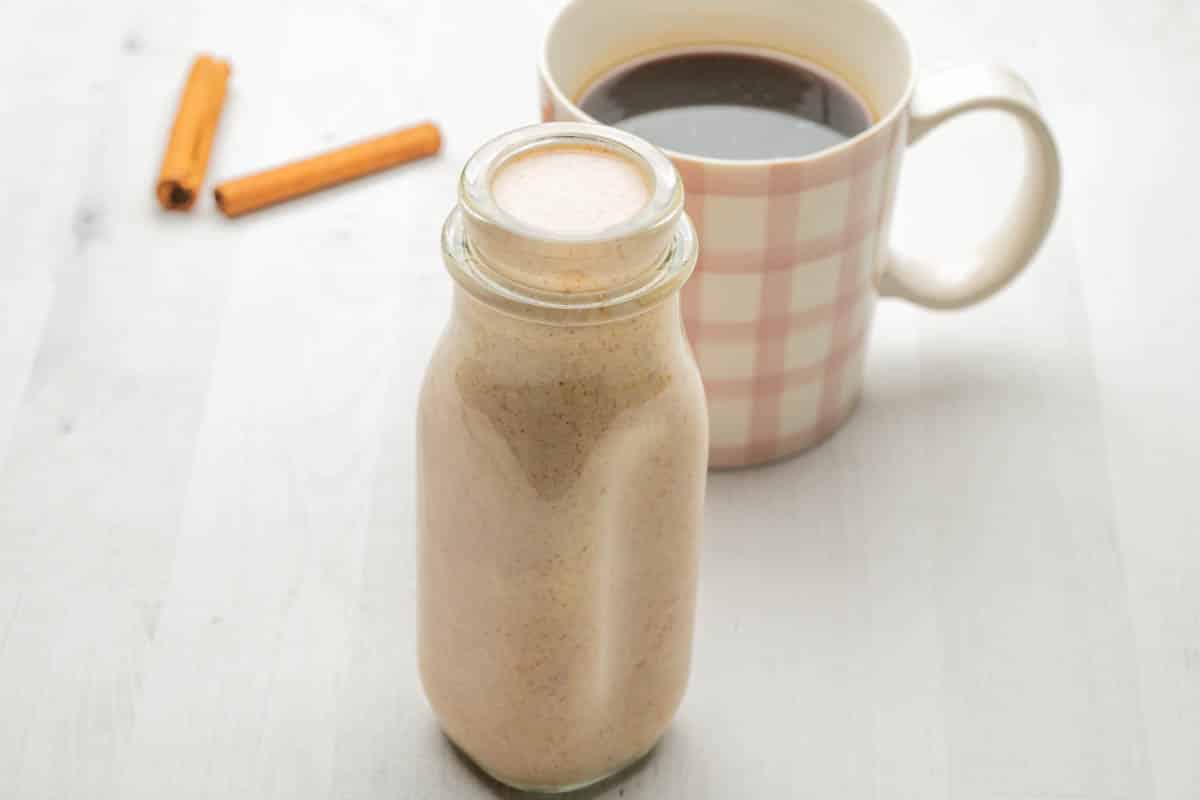 A pink plaid cup of coffee with cinnamon coffee creamer and a glass storage jar.