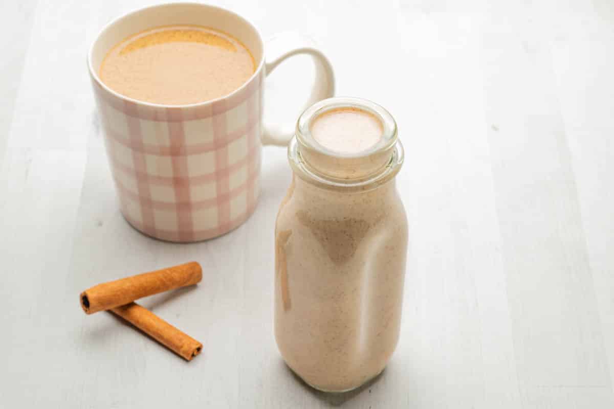 A pink plaid cup of coffee with cinnamon coffee creamer and a glass storage jar.