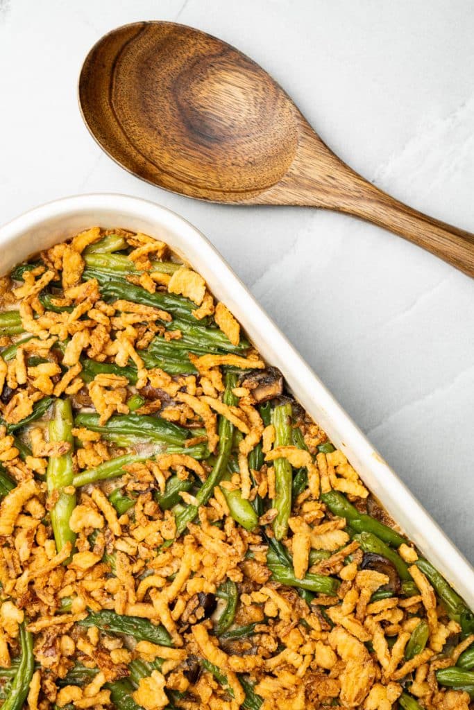 An overhead view of fresh green bean casserole in a baking dish with a wooden spoon.