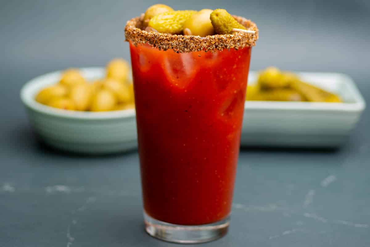 A virgin Bloody Mary mocktail in a pint glass with a small skewer of dill pickles and olives.