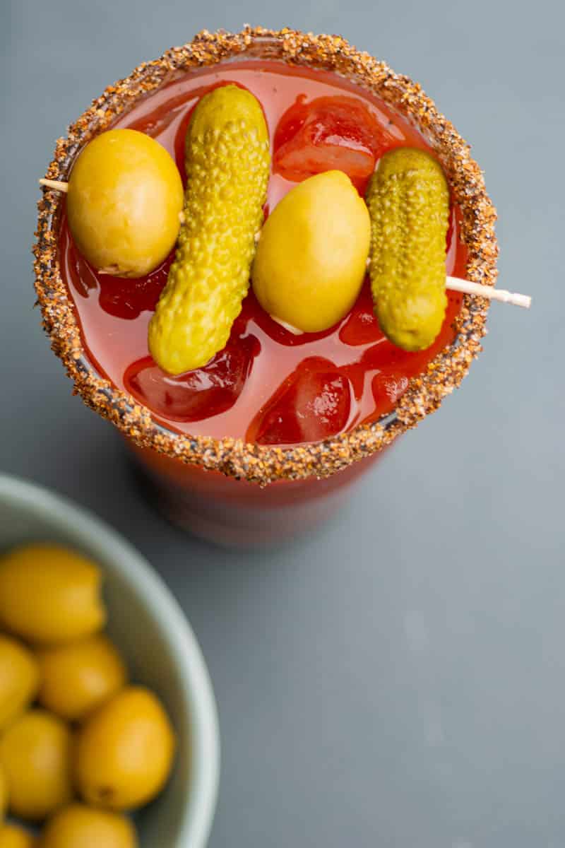 An overhead view of a skewer of pickles and olives on the top of a pint glass.