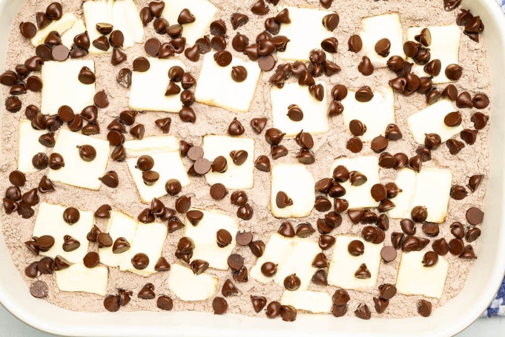 Chocolate chips, chocolate cake mix, and butter slices in a baking dish.