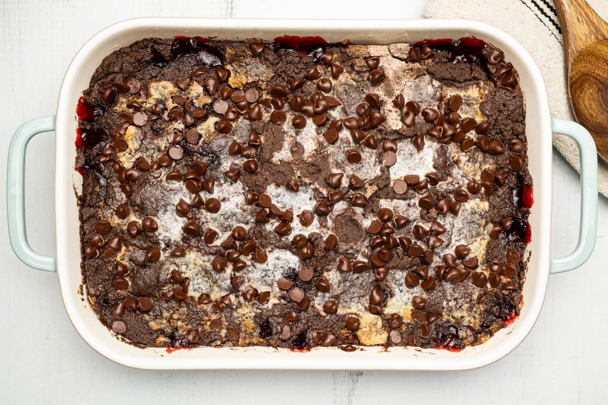 Chocolate cherry dump cake in a sea salt green baking dish with a wooden spoon.