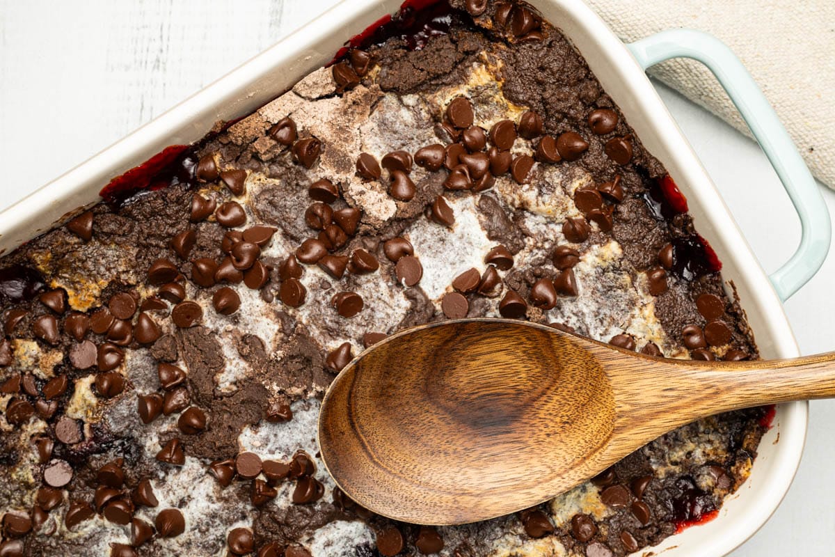Chocolate cherry dump cake in a sea salt green baking dish with a wooden spoon.