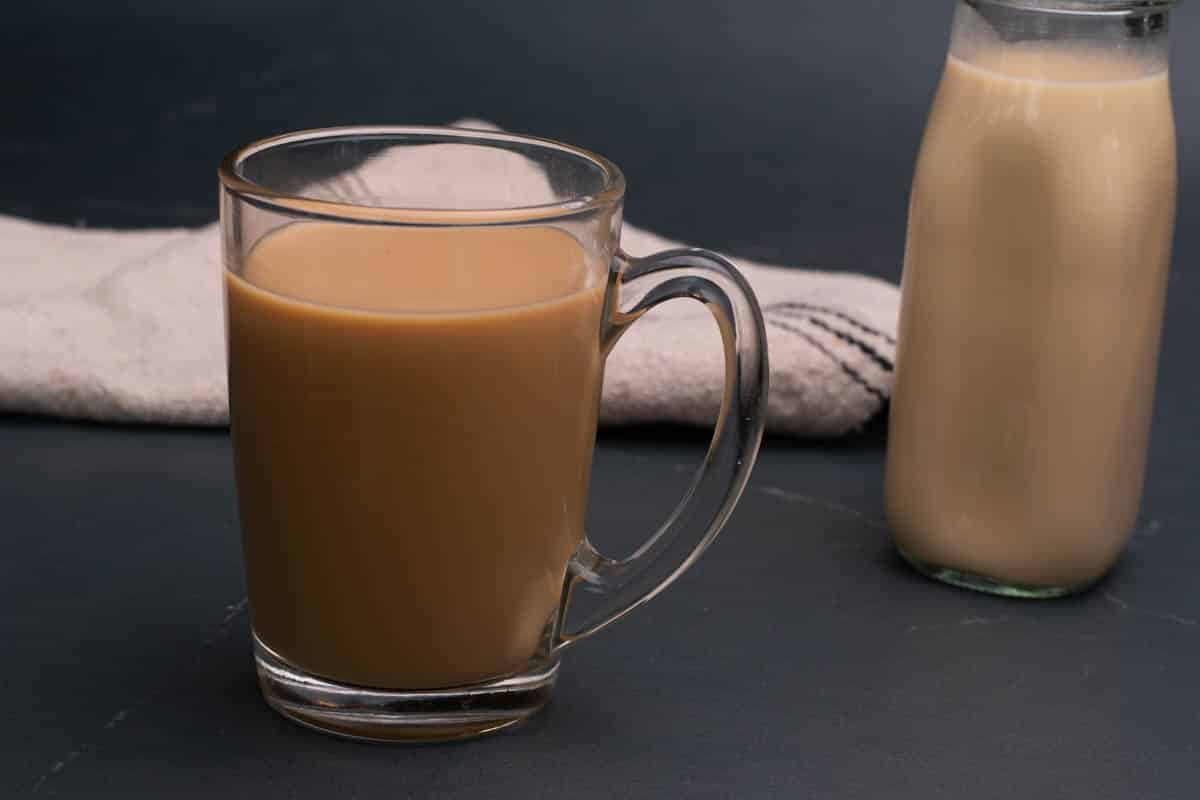 A glass jar with homemade salted caramel coffee creamer and a cup of a homemade coffee drink.