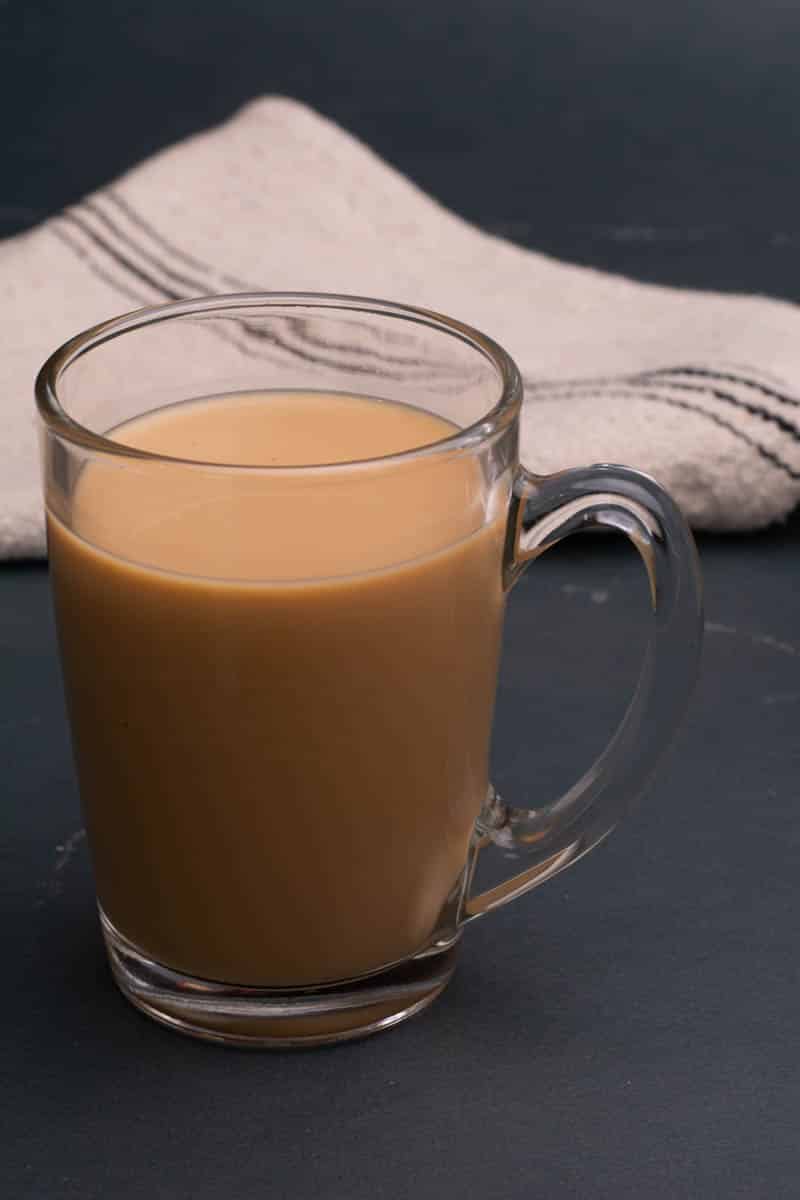 A glass cup of coffee with a towel in the background on a dark table.