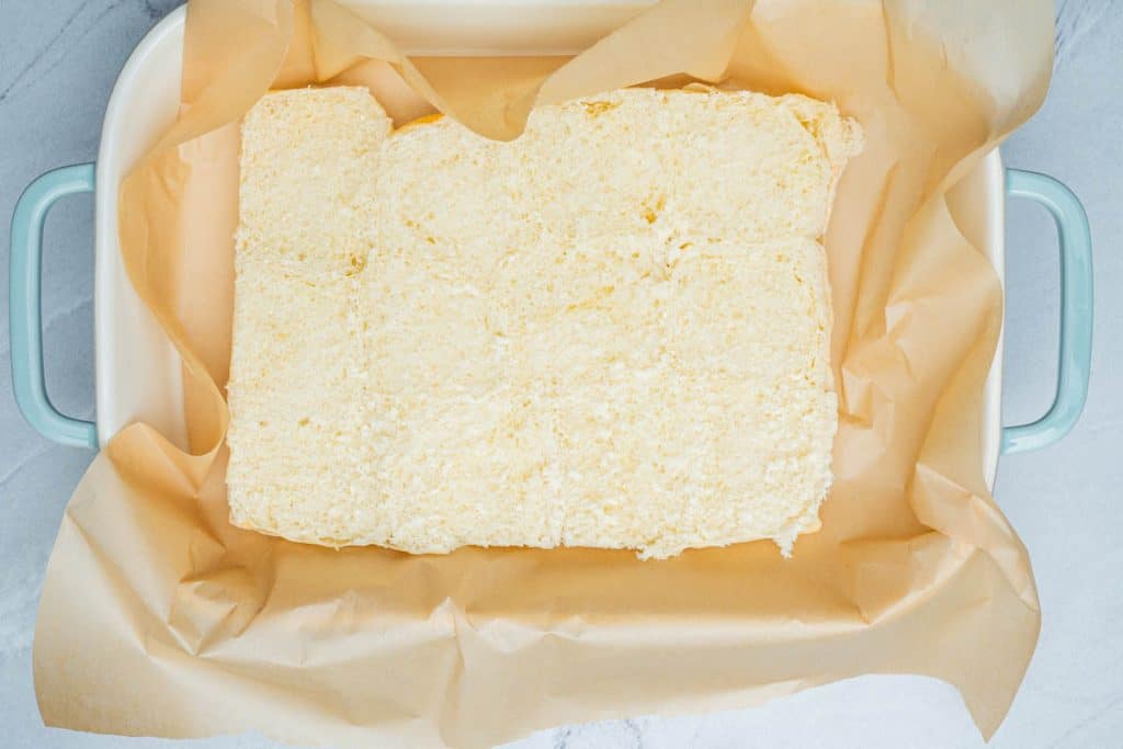 The bottom half of Hawaiian rolls in a parchment paper lined baking dish.