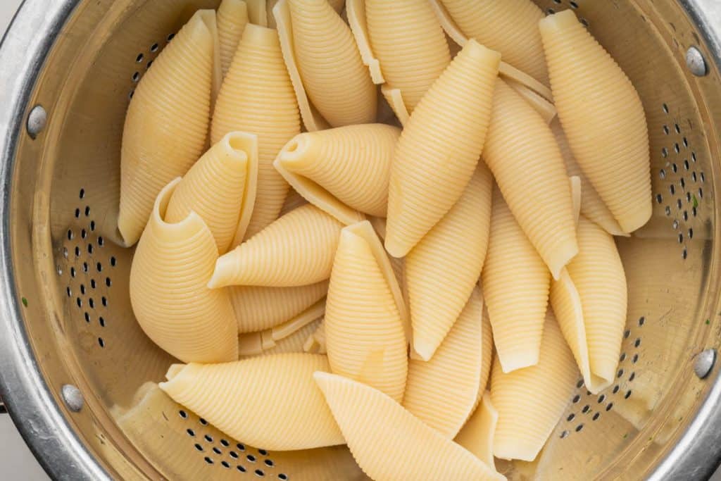 A colander filled with cooked jumbo pasta shells.