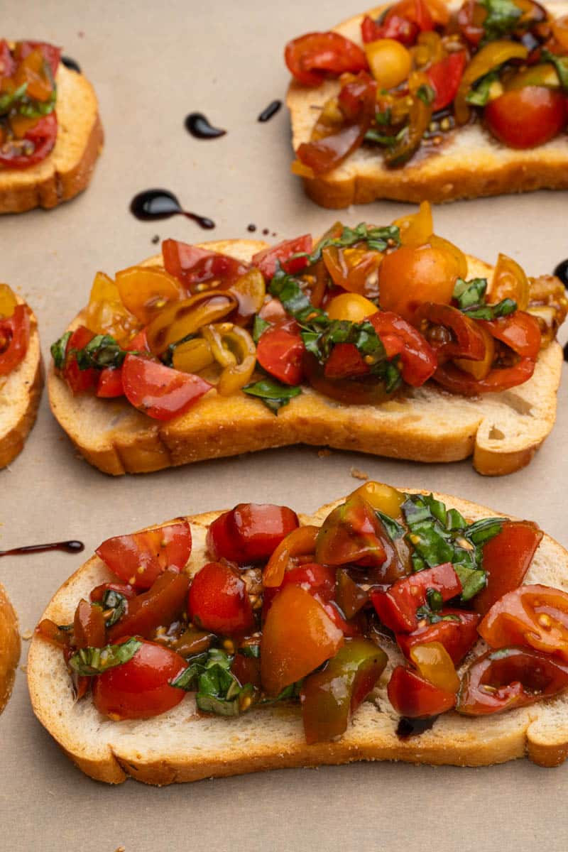 Balsamic bruschetta on crostini drizzled with balsamic glaze on parchment paper.