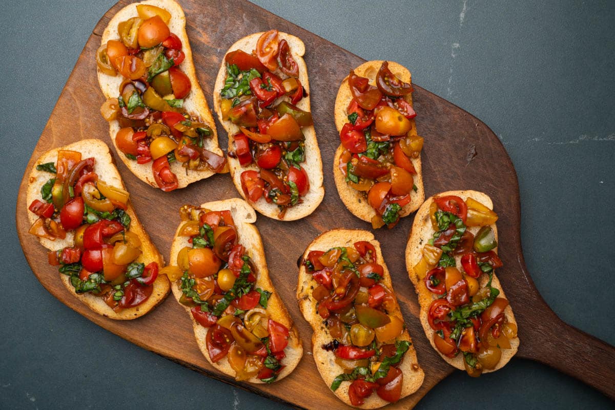 Overhead photo of balsamic bruschetta on crostini placed on a wooden serving board.