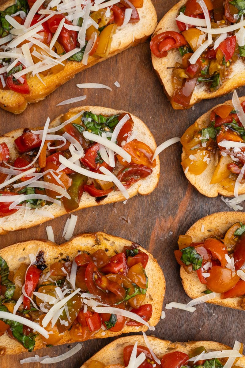 Balsamic bruschetta on a crostini topped with shredded parmesan on a wooden board.