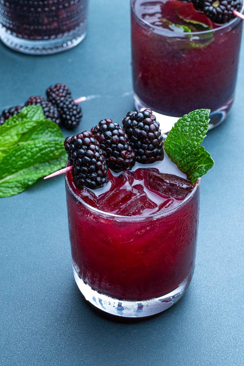 Two glasses of blackberry bourbon smash with a cocktail shaker and skewers of blackberries.
