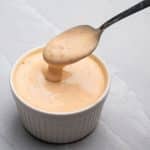 Sriracha aioli in a white bowl with a spoon dipping in the sauce.