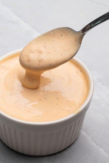 Sriracha aioli in a white bowl with a spoon dipping in the sauce.