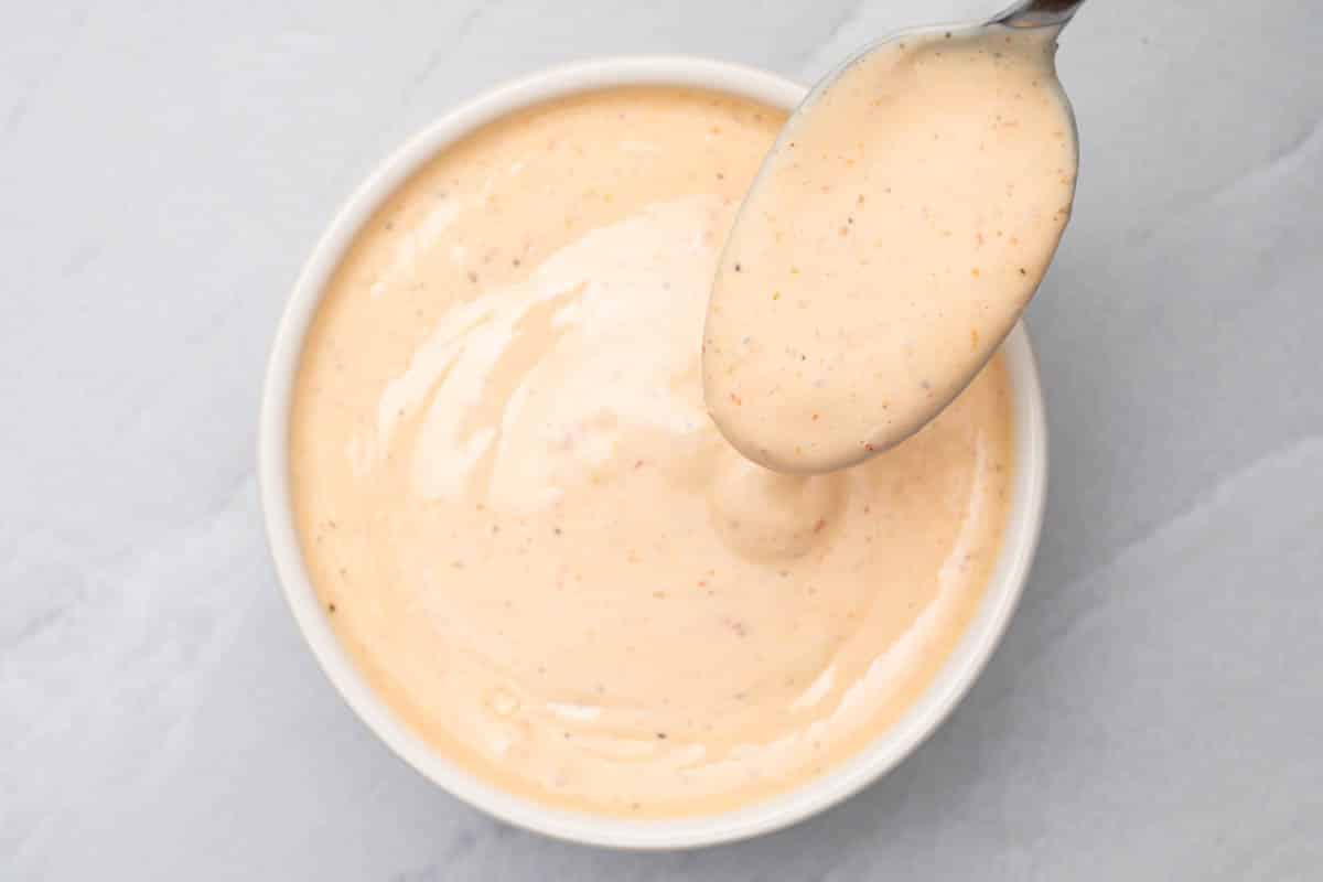 Sriracha aioli in a white bowl with a spoon dipping in the sauce.