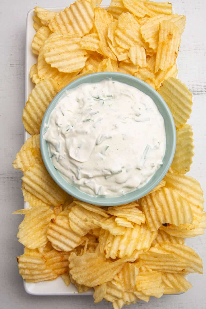 Overhead photo of a bowl of sour cream and chive dip with ruffled potato chips.