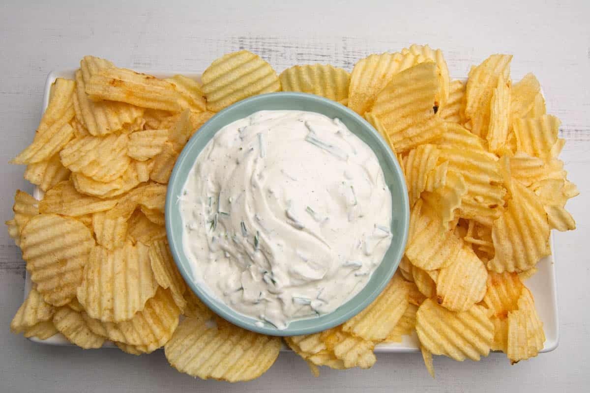 A rectangular plate full of ruffled potato chips and sour cream and chive dip.